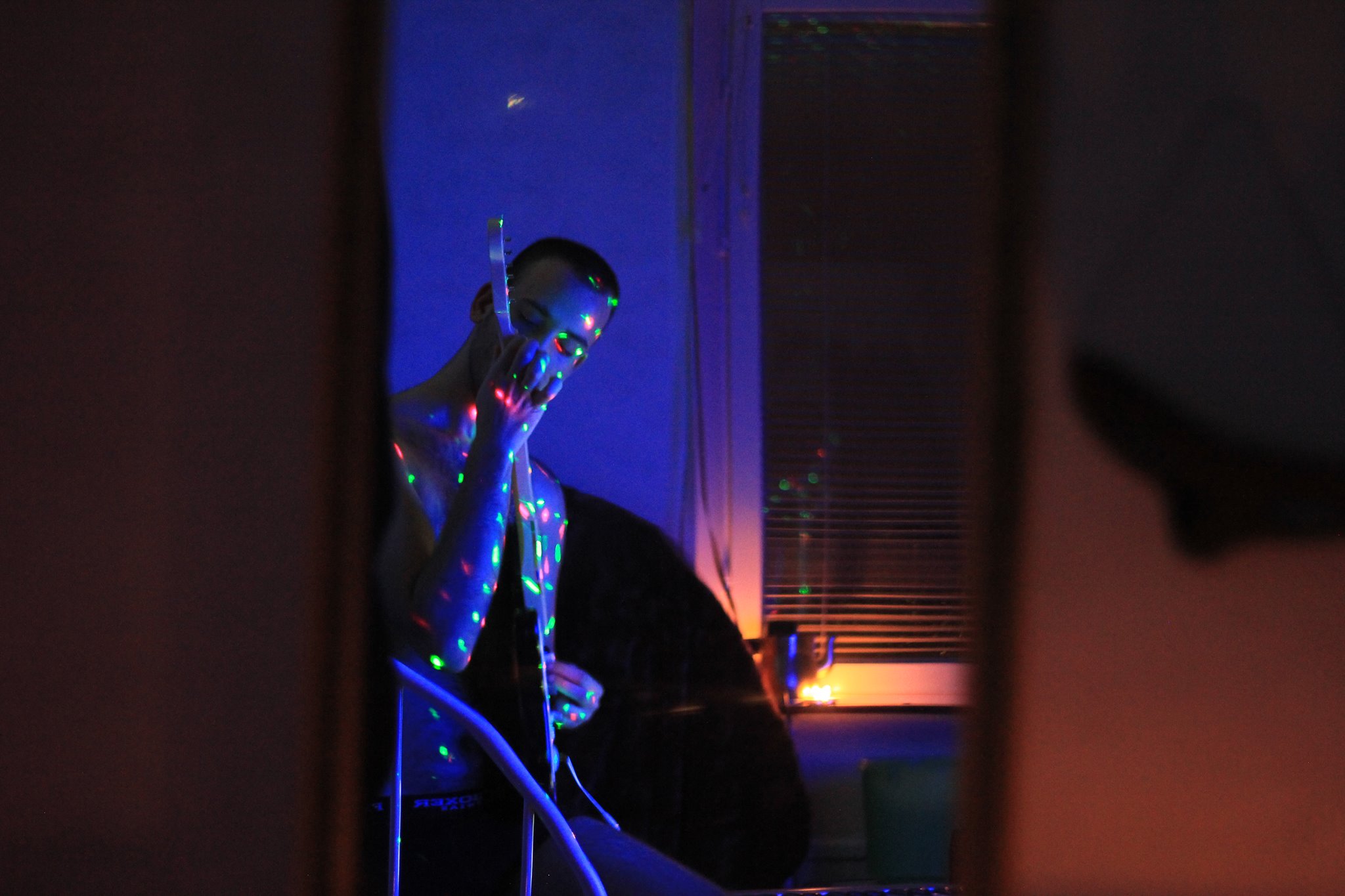 An image of me from 2014, playing a music rhythm game with a guitar, illuminated by candlelight and laser beams